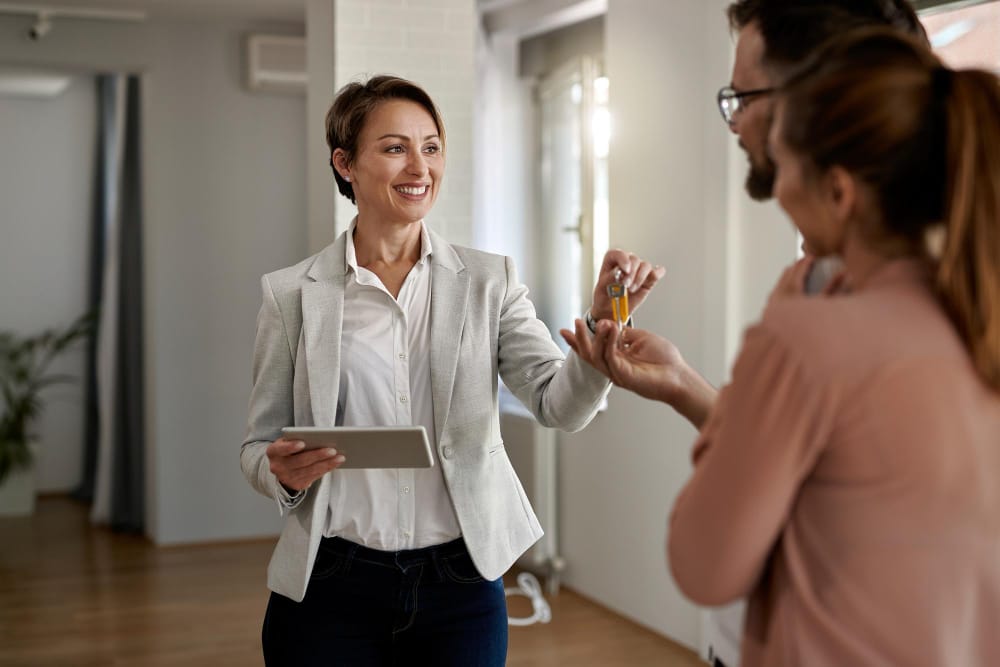 Agente immobilière souriante remettant les clés d'un nouvel appartement à un couple de nouveaux propriétaires.
