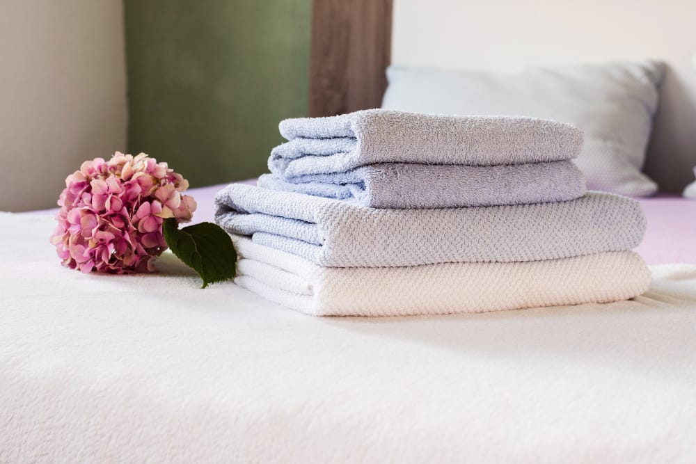 Pile de serviettes de bain propres, empilées sur un lit d'hôtel à côté d'une fleur d'hortensia rose et lilas
