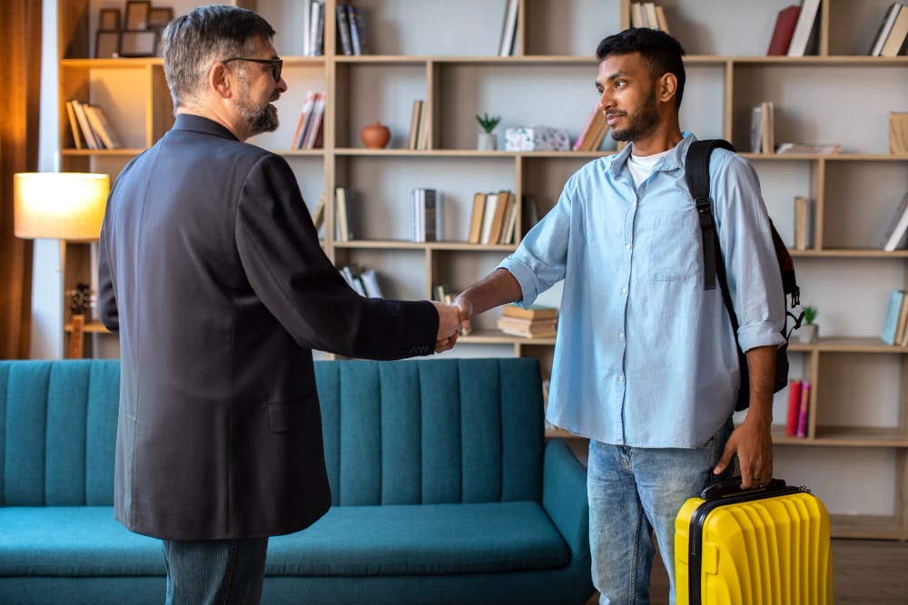 Poignée de main entre un homme d'affaires et un jeune voyageur avec un sac à dos et une valise jaune dans un hall d'entrée.