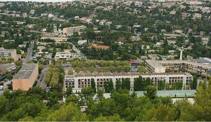 Vue aérienne et panoramique de Carnoux-en-Provence, montrant les maisons, la pinède et les collines méditerranéennes sous le soleil.