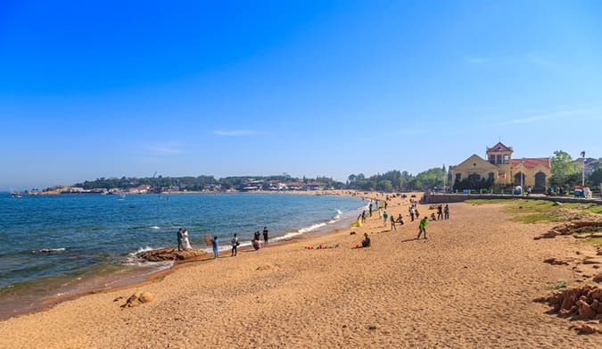 Vue panoramique de la plage de Saint-Cyr, avec sable fin, mer calme et promeneurs près du rivage et d'un bâtiment historique.