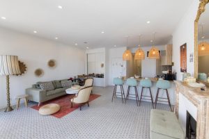 Appartement contemporain avec salon ouvert, bar de cuisine avec chaises hautes bleues et cheminée décorative en marbre.