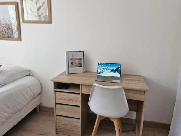 Bureau de travail en bois clair avec ordinateur portable dans une chambre moderne d'appartement de location.
