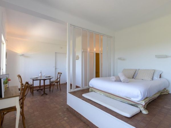 Chambre d'hôtel ou studio moderne avec un grand lit double sur estrade et une petite table ronde pour les repas.