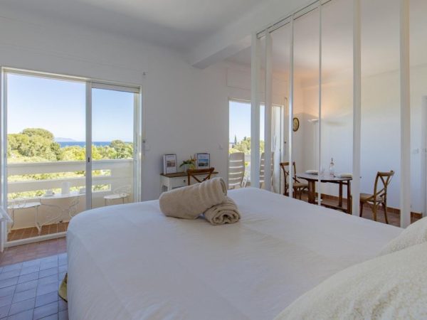 Chambre d'hôtel avec vue mer et balcon, lit double blanc et porte-fenêtre donnant sur la Méditerranée.