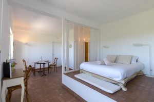 Studio moderne avec lit double sur estrade séparé par une cloison vitrée et un petit coin repas.