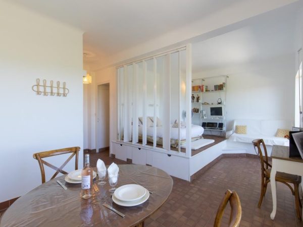 Studio moderne avec coin repas et lit double surélevé séparé par une cloison ajourée, idéal pour un appartement de vacances.